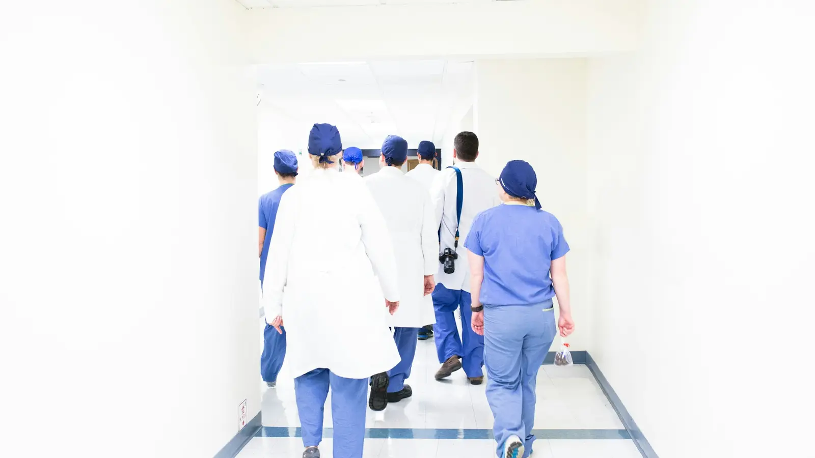 A team of clinicians in scrubs walks together down a bright hospital corridor