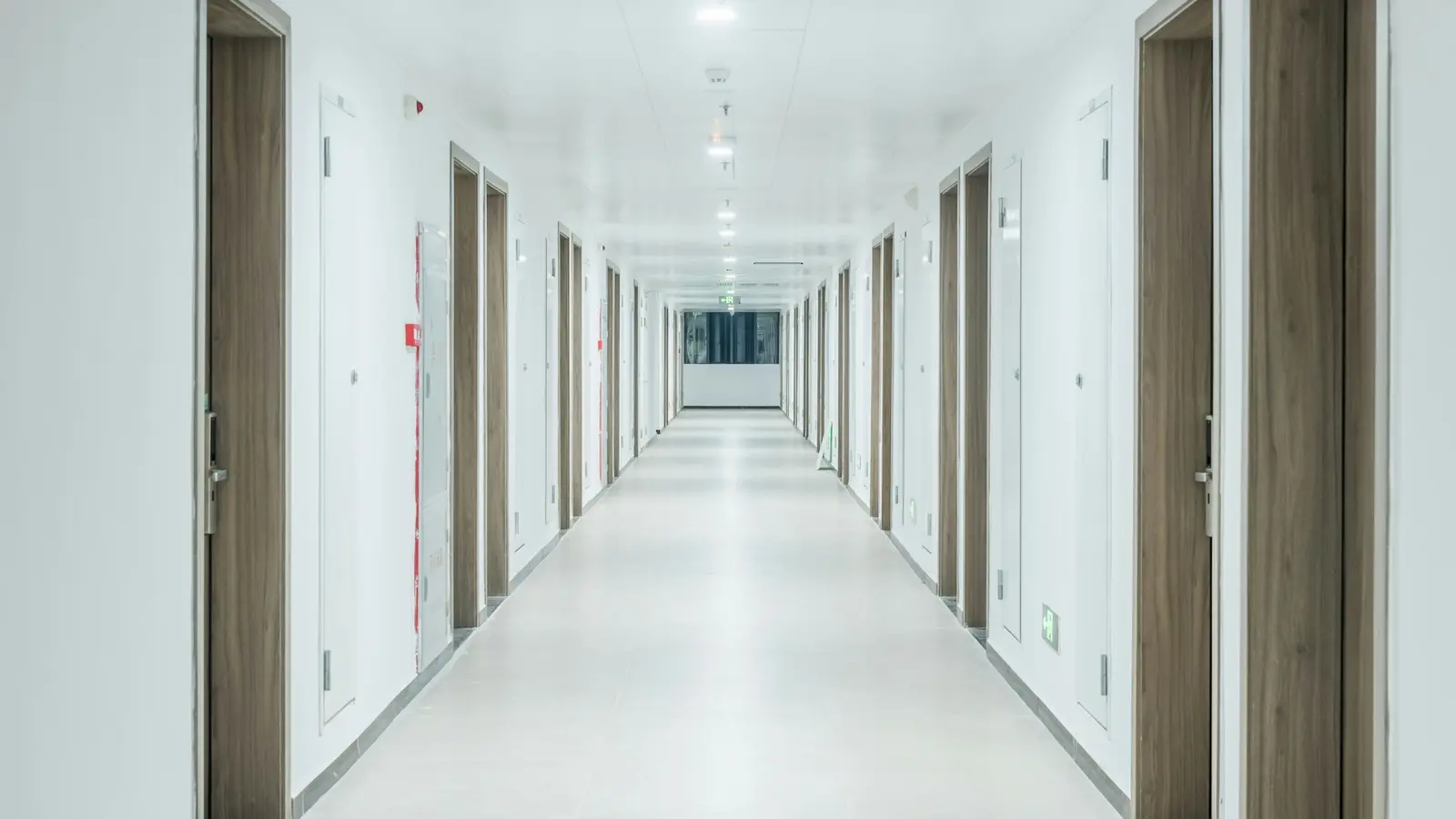 A long hospital corridor with rows of doors under even light