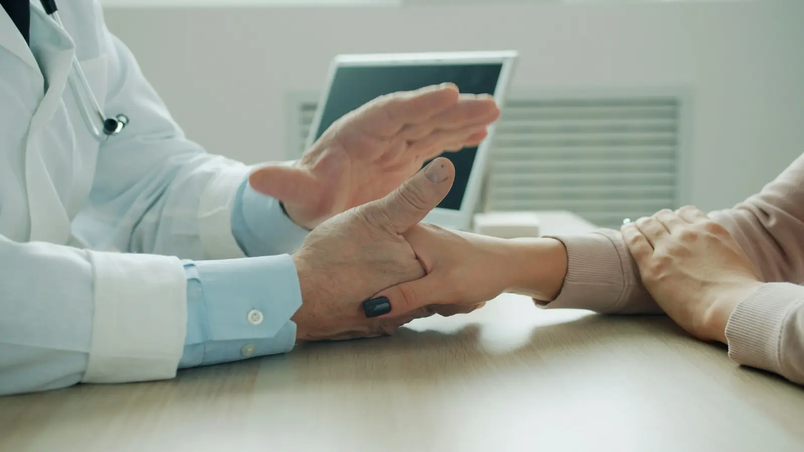 A clinician holds a tablet while sitting with an older patient, their hands in focus