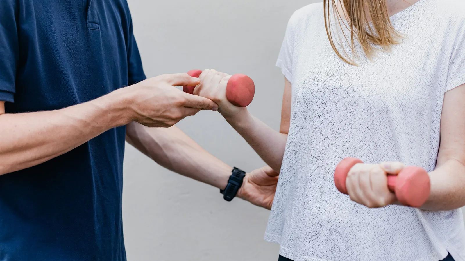 A physiotherapist guides a patient's arm through a light dumbbell exercise in a rehabilitation session