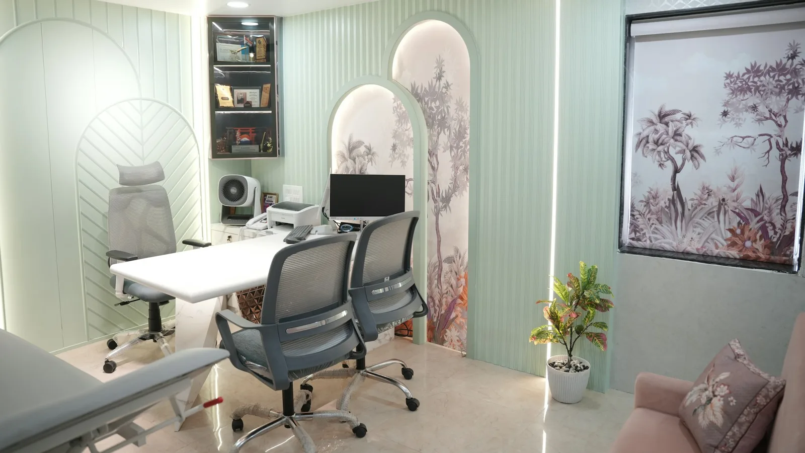 A specialist consulting room in soft mint tones with a desk, chairs and an examination couch