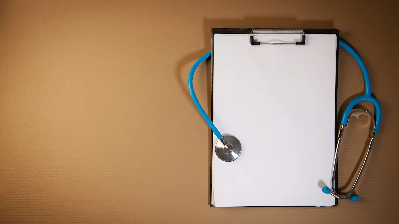 A clipboard and blue stethoscope arranged on a plain desk
