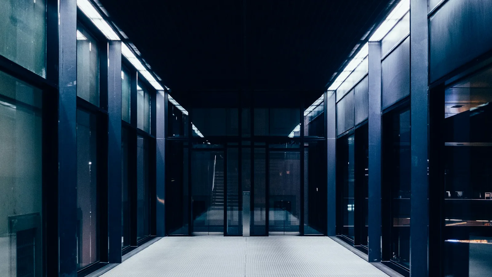 A dimly lit data centre aisle running between rows of glass-fronted server cabinets under cool overhead lighting