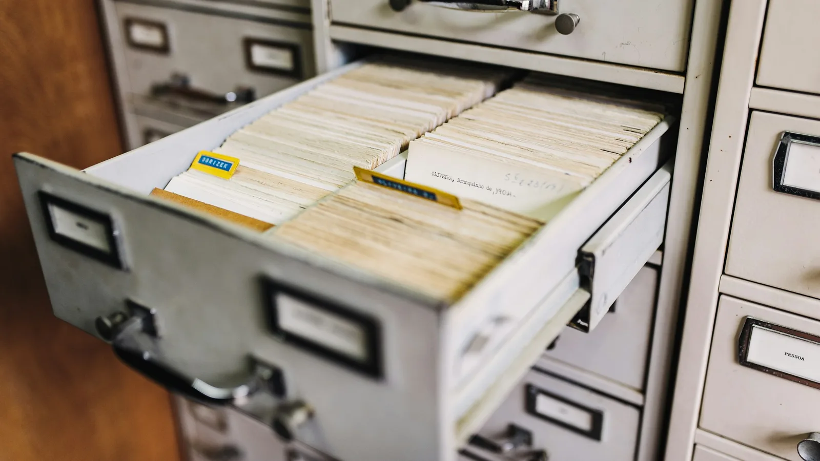 An open drawer of a metal filing cabinet packed with aged index cards and paper records