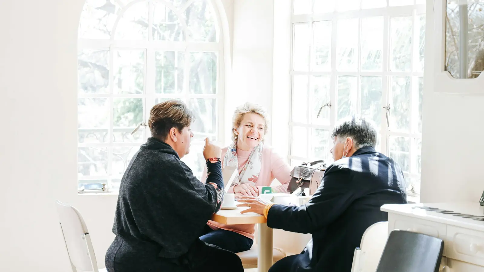 A small clinic team talks around a wooden table in a bright, naturally lit practice meeting room